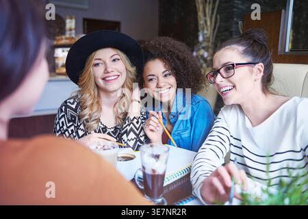 Verschiedene Gruppe weiblicher Freunde, die sich miteinander unterhalten, während sie am Tisch mit Getränken im Café sitzen Stockfoto