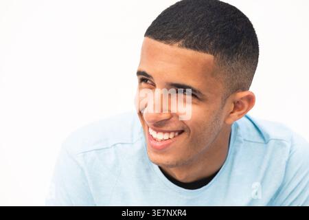 Lächelnder arabischer männlicher Teenager, der wegschaut und sich vor weißem Hintergrund stützt Stockfoto