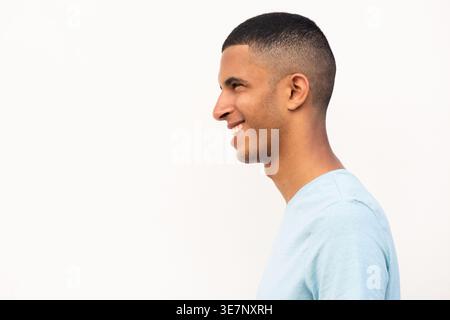 Lächelnder arabischer männlicher Teenager, der seitlich vor weißem Hintergrund wegschaut Stockfoto