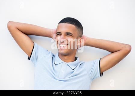 Lächelnder arabischer männlicher Teenager, der wegschaut, mit Händen hinter dem Kopf vor weißem Hintergrund Stockfoto