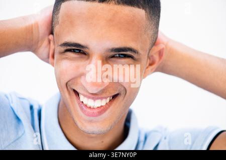 Lächelnder arabischer männlicher Teenager, der mit Händen hinter dem Kopf vor weißem Hintergrund steht Stockfoto