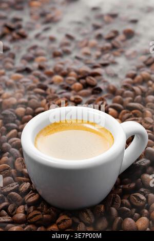 Frisch gebrühter Espresso in einer weißen Tasse, reichhaltige Crema bildet sich oben, umgeben von gerösteten Kaffeebohnen mit aufsteigendem Dampf Stockfoto