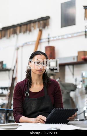 Gemischte Frau mit Twist, die eine Schutzbrille trägt und am Arbeitsplatz steht Stockfoto