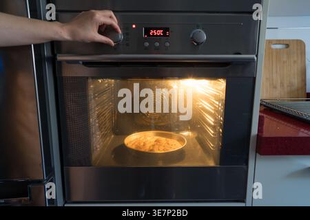 Frau, die die Temperatur eines Ofens anpasst, um köstliche hausgemachte Focaccia zu backen. Die Kücheneinrichtung umfasst ein hölzernes Schneidebrett und eine gut beleuchtete Ove Stockfoto