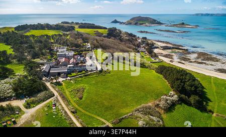 Blick aus der Vogelperspektive auf Herm Island Dorf und Farmland mit Küstenbucht und felsigen Inselchen, Kanalinseln Stockfoto