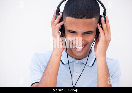 Lächelnder arabischer männlicher Teenager mit Kopfhörern, die vor weißem Hintergrund stehen Stockfoto