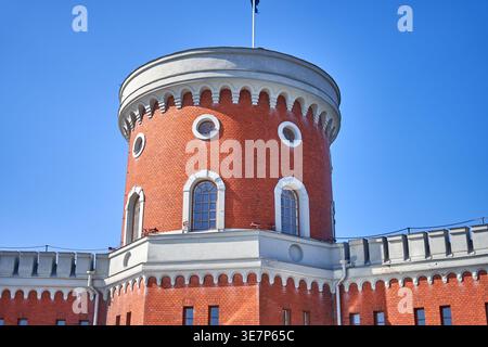 Niedrig angefertigte Ansicht eines historischen roten Backstein-Fortificationsturms mit weißem Steinarchitekturbesatz vor einem klaren blauen Himmel. Der zylindrische Turm zeigt Stockfoto