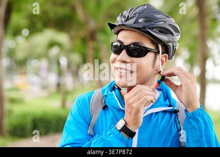Lächelnder asiatischer Radfahrer mit Sonnenbrille und Fahrradhelm im Park Stockfoto