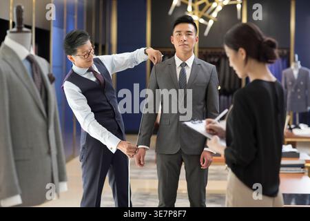 Chinesische Modedesigner messen männliche und weibliche chinesische Kunden, während sie in der Modeboutique stehen Stockfoto