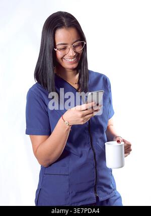 Hispanische Krankenschwester mit Smartphone, die Kaffeetasse vor weißem Hintergrund hält Stockfoto