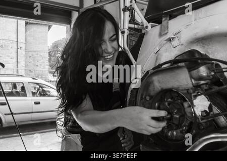 Lächelnde hispanische Mechanikerin repariert Autoteile in der Autowerkstatt Stockfoto