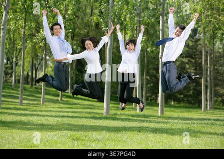Chinesische Männer und Frauen, die ihre Arme heben, springen zusammen im Park an sonnigen Tagen Stockfoto