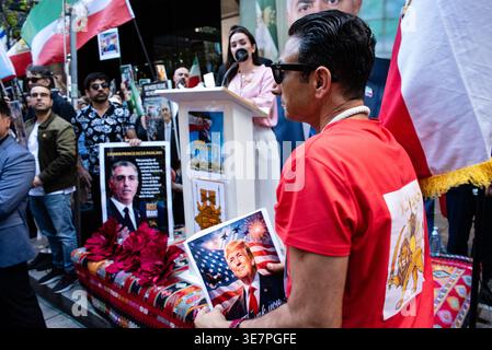 North Sydney, Australien. April 2026. Ein Mann läuft am Rednerpult vorbei mit einem Poster des US-Präsidenten Donald Trump, auf dem auf einer Kundgebung vor dem US-Generalkonsulat in der Miller Street 50 in North Sydney „Danke“ steht. Die Kundgebung ist Teil eines koordinierten globalen Aktionstages, der von Teilen der iranischen Diaspora zur Unterstützung des ehemaligen Kronprinzen Reza Pahlavi organisiert wird. Quelle: Sergio Leyva Seiglie/Alamy Live News Stockfoto