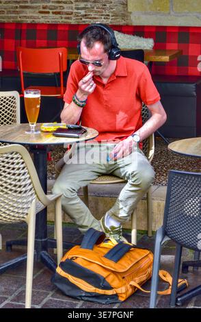 Alleinstehender Mann/Tourist auf der Terrasse des Cafés mit einem Glas Bier und Kopfhörern - Tours, Indre-et-Loire (37), Frankreich. Stockfoto