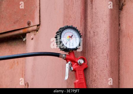 Ein an einer Wand angebrachtes Manometer misst den Reifendruck. Das Manometer zeigt die aktuellen Druckwerte in einem Lagerbereich mit Gitterhintergrund an. Stockfoto