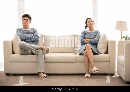 Chinesisches Paar, das mit einem Sitzplatz auseinander auf dem Sofa im Wohnzimmer zu Hause sitzt Stockfoto