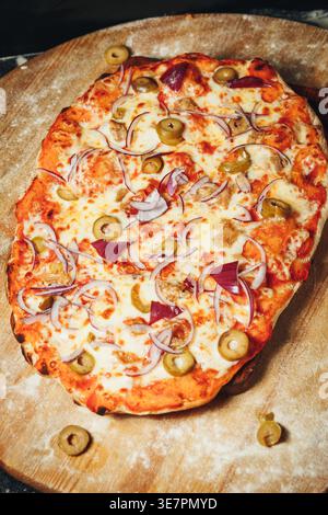 Traditionelle italienische Pinsa romana mit Tomatensauce geschmolzener Mozzarella, pikanten Pilzen und dünnen Scheiben Schinken auf einem bemehlten Holz Stockfoto