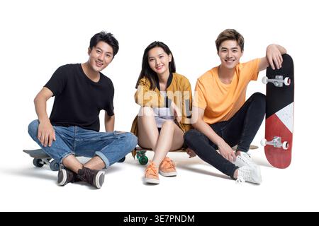 Lächelnde chinesische Freunde sitzen auf Skateboards vor weißem Hintergrund im Studio Stockfoto
