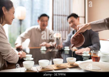 Eine Chinesin führt eine Teezeremonie vor und sitzt mit Freunden im Teeraum am Tisch Stockfoto