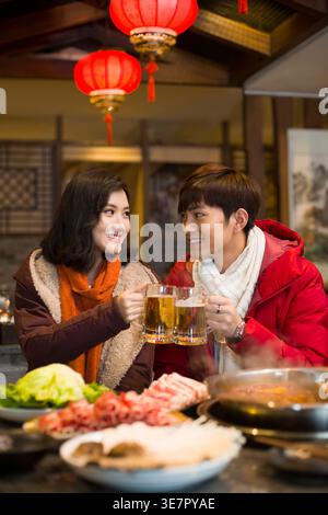 Ein chinesisches Paar, das sich ansieht, wie er Gläser Bier am Tisch im Hotpot-Restaurant toast Stockfoto