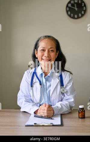 Asiatische Oberärztin mit gefesselten Händen am Tisch in der Klinik Stockfoto