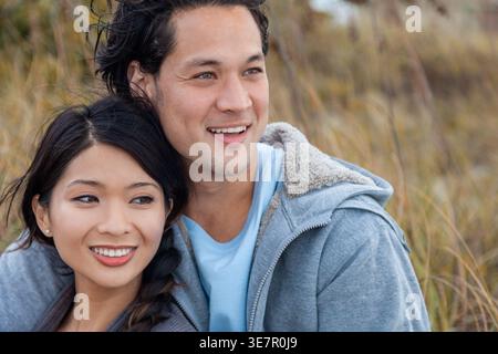 Lächelndes asiatisches Paar, das bei einem romantischen Date im Freien nahe beieinander sitzt Stockfoto