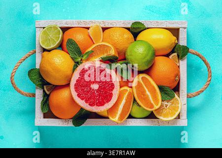 Frische Zitrusfrüchte mit Blättern: Zitronen, Orangen, Mandarinen, Grapefruit, Limette in Holzkiste, Draufsicht. Stockfoto