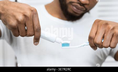 Schwarzer Mann, der Zahnpasta auf die Zahnbürste im Badezimmer zu Hause aufträgt Stockfoto