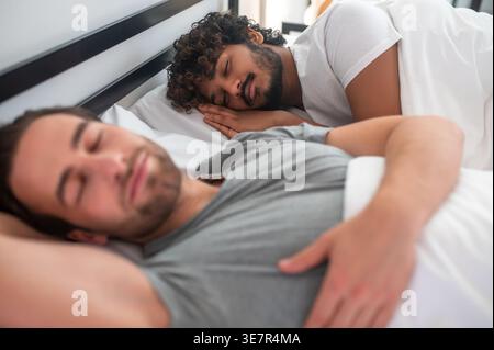 Indische und kaukasische Schwule schlafen zusammen im Bett zu Hause Stockfoto
