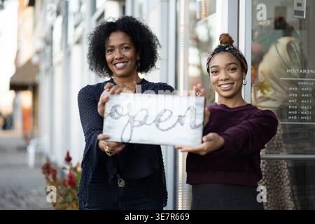 Lächelnde afroamerikanische Frauen halten ein Schild an der Eingangstür offen Stockfoto