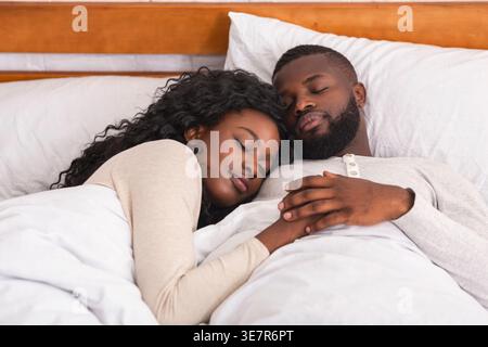 Ein schwarzes Paar, das sich umschließt, während es im Schlafzimmer zu Hause auf dem Bett liegt Stockfoto