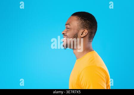 Schwarzer Mann, der wegschaut und seitlich vor der blauen Wand im Studio steht Stockfoto