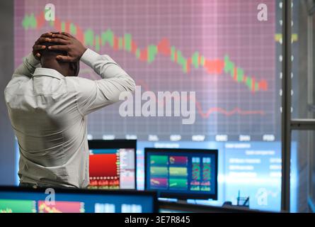 Enttäuschter schwarzer männlicher Broker, der den Kopf berührt und die Grafik im Börsenhandelsbüro abnimmt Stockfoto