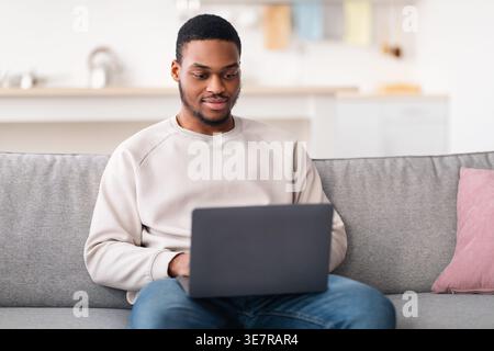 Schwarzer männlicher Freelancer, der zu Hause im Wohnzimmer auf der Couch sitzt Stockfoto
