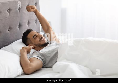 Ein arabischer Mann, der die Arme ausdehnt, während er zu Hause im Bett liegt Stockfoto