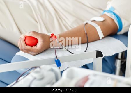 Schwarzer Frauenarm mit rotem Herz-Squeeze-Ball, der Blut spendet, liegt auf dem Krankenhausbett in der Klinik Stockfoto