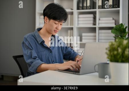 Asiatischer Geschäftsmann, der am Laptop arbeitet, während er im Büro am Tisch sitzt Stockfoto