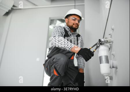 Indischer Klempner mit Uniform und Schutzhelm, der Wasserausrüstung im Badezimmer installiert Stockfoto