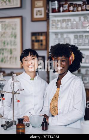 Japanische und schwarze Apothekerinnen stehen zusammen an der Theke in einer Vintage-Apotheke Stockfoto