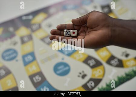 Hände des Schwarzen Mannes, der Würfel hält, während er am Tisch mit Brettspiel in der Universitätsbibliothek steht Stockfoto