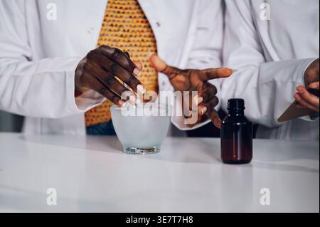 Zugeschnittenes Bild von schwarzen Apothekerinnen, die Pissel halten, die neben einer japanischen Kollegin stehen, die eine Karte in einer Vintage-Apotheke hält Stockfoto