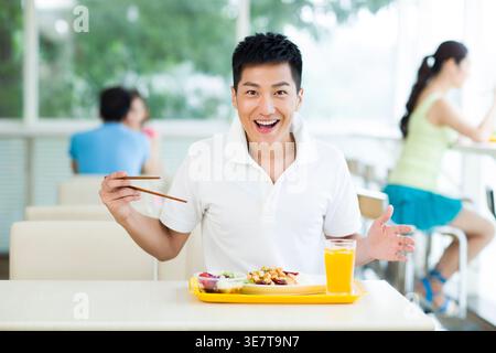 Fröhlicher Chinese, der Essstäbchen beim Essen benutzt, während er am Tisch im Restaurant sitzt Stockfoto