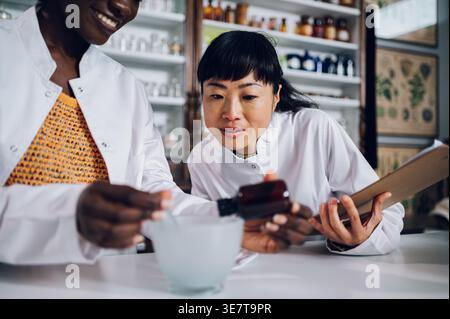 Fokussiertes japanisches Pharmazeutik-Monitoring-Experiment von schwarzer Kollegin mit Mörtel und Zutaten aus Glasflaschen, die in Vintage-Phaar stehen... Stockfoto