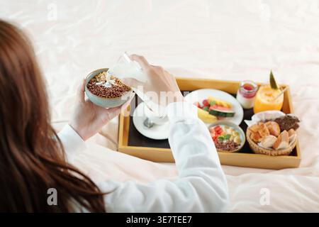 Hände einer asiatischen Frau, die Müsli mit frischem Joghurt, Beeren und Früchten hält und auf dem Bett mit Frühstückstablett im Hotelzimmer sitzt Stockfoto