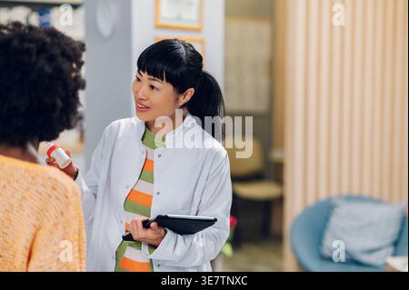 Japanische Apothekerin mit Salbenspender und Klemmbrett, die mit schwarzer Patientin und Kundin in der Apotheke spricht Stockfoto
