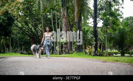 Asiatische Frau, die tagsüber mit sibirischem Huskyhund im Park läuft Stockfoto