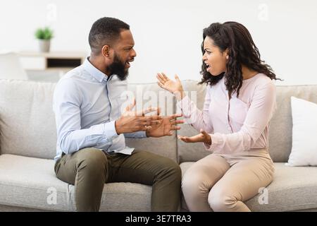 Schwarzes Paar, das sich anschreit und streitet, während es auf dem Sofa zu Hause im Wohnzimmer sitzt Stockfoto