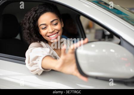 Schwarze Frau, die den Seitenspiegel verstellt, während sie auf dem Beifahrersitz sitzt Stockfoto
