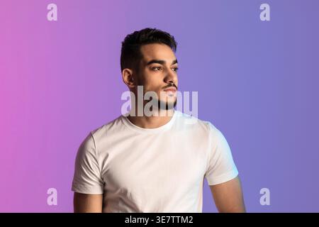 Ein arabischer Mann mit Bart, der ein weißes Hemd trägt, der im Studio vor rosa und violettem Farbverlauf steht Stockfoto