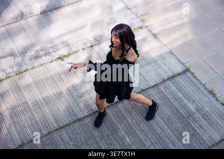 Von oben Blick auf die Schwarze Frau, die an sonnigen Tagen ein schwarzes Minikleid mit Dreiviertelärmeln trägt Stockfoto